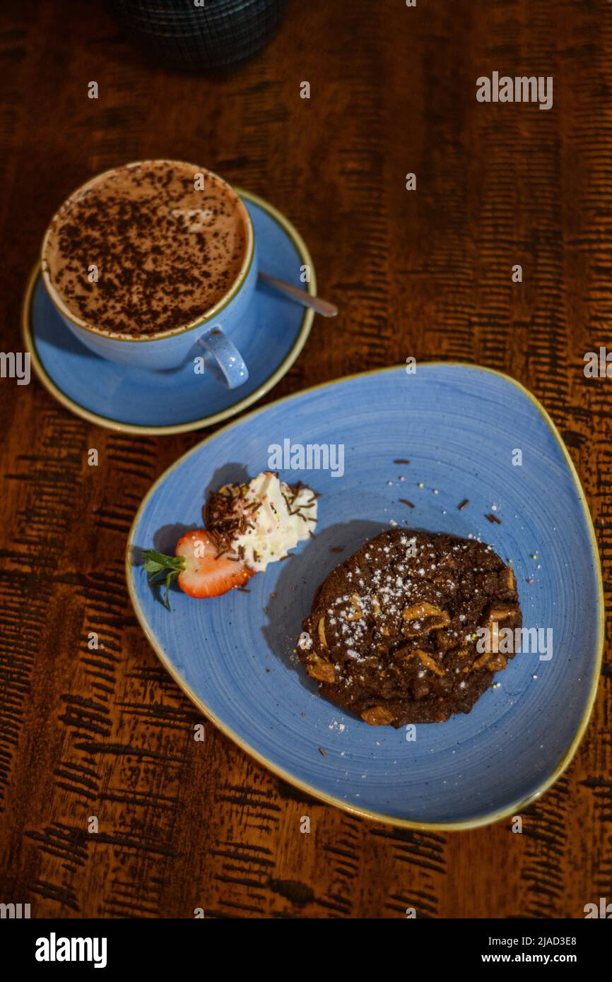 Blick von oben auf ein Schokoladen- und Nusskekse mit einer heißen Schokolade auf einem Tisch Stockfoto