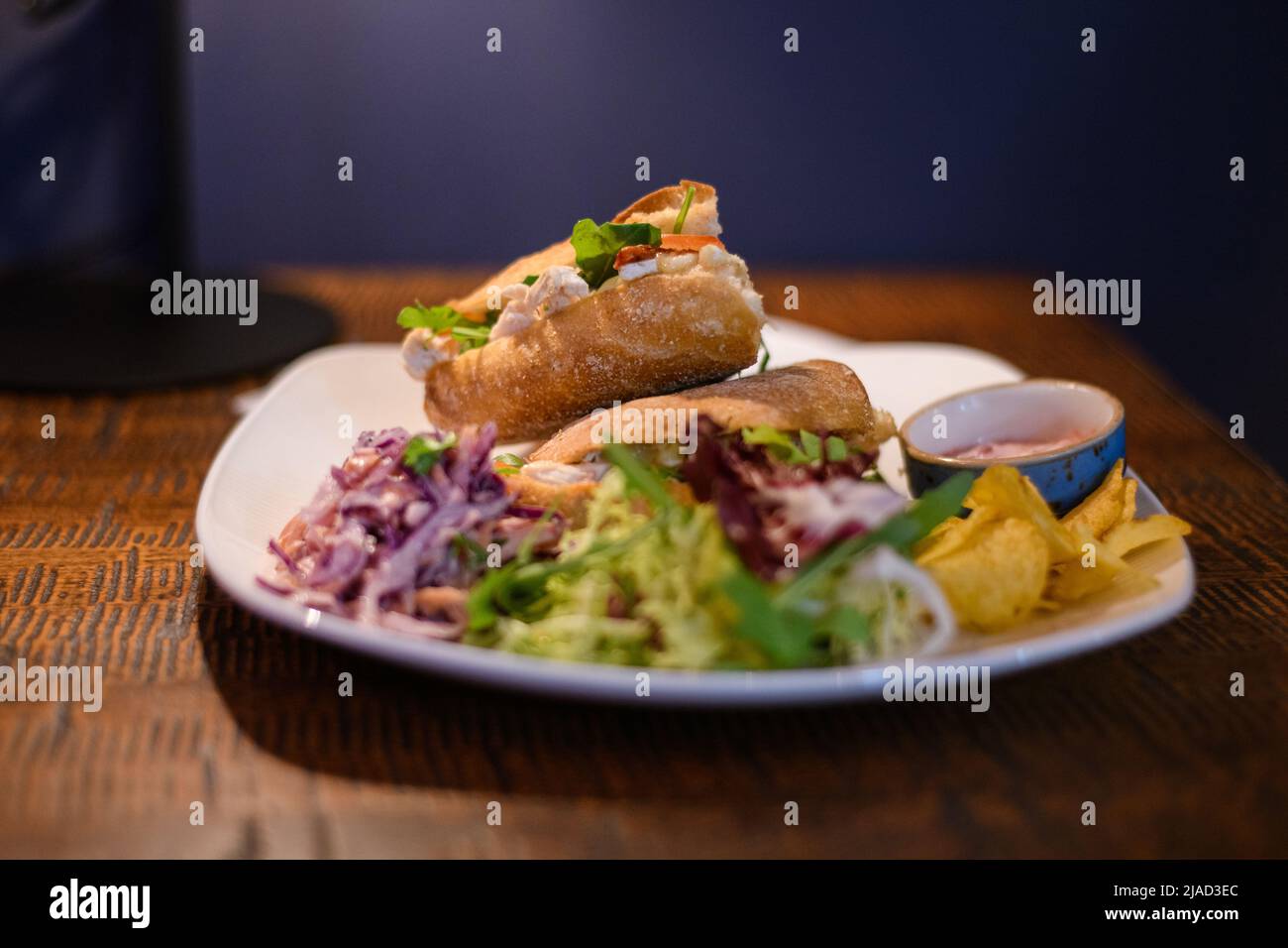 Nahaufnahme von Hähnchen-, Brie- und Salat-Sandwiches mit Krautsalat, grünem Salat und Chips Stockfoto