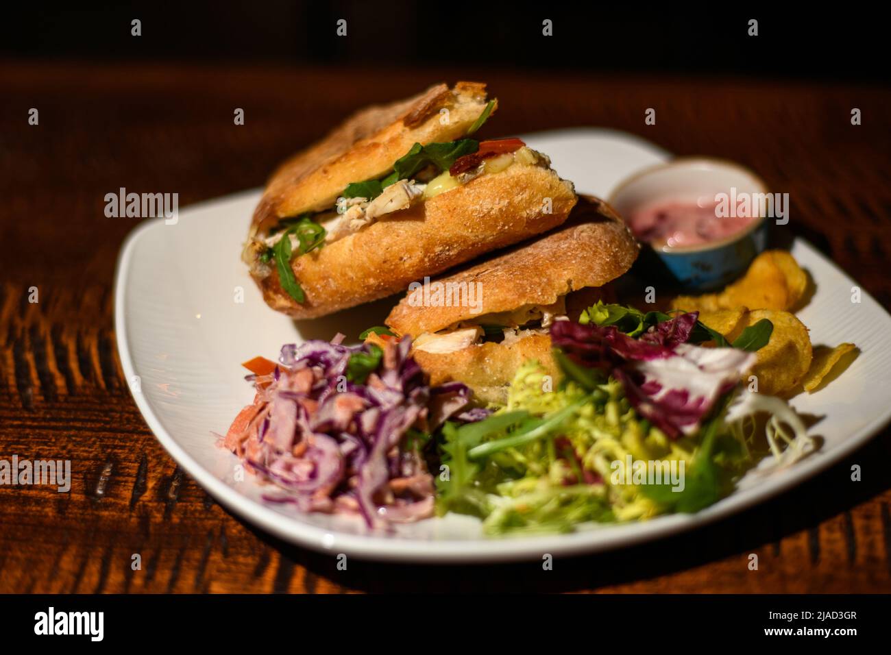 Nahaufnahme von Hähnchen-, Brie- und Salat-Sandwiches mit Krautsalat, gemischtem grünen Salat und Chips Stockfoto