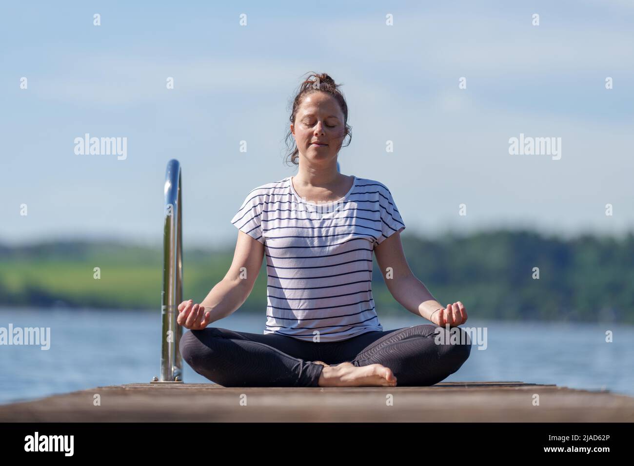 Frau, die mit gekreuzten Beinen auf einem Dock sitzt und meditiert, Wallersee, Salzburg, Österreich Stockfoto