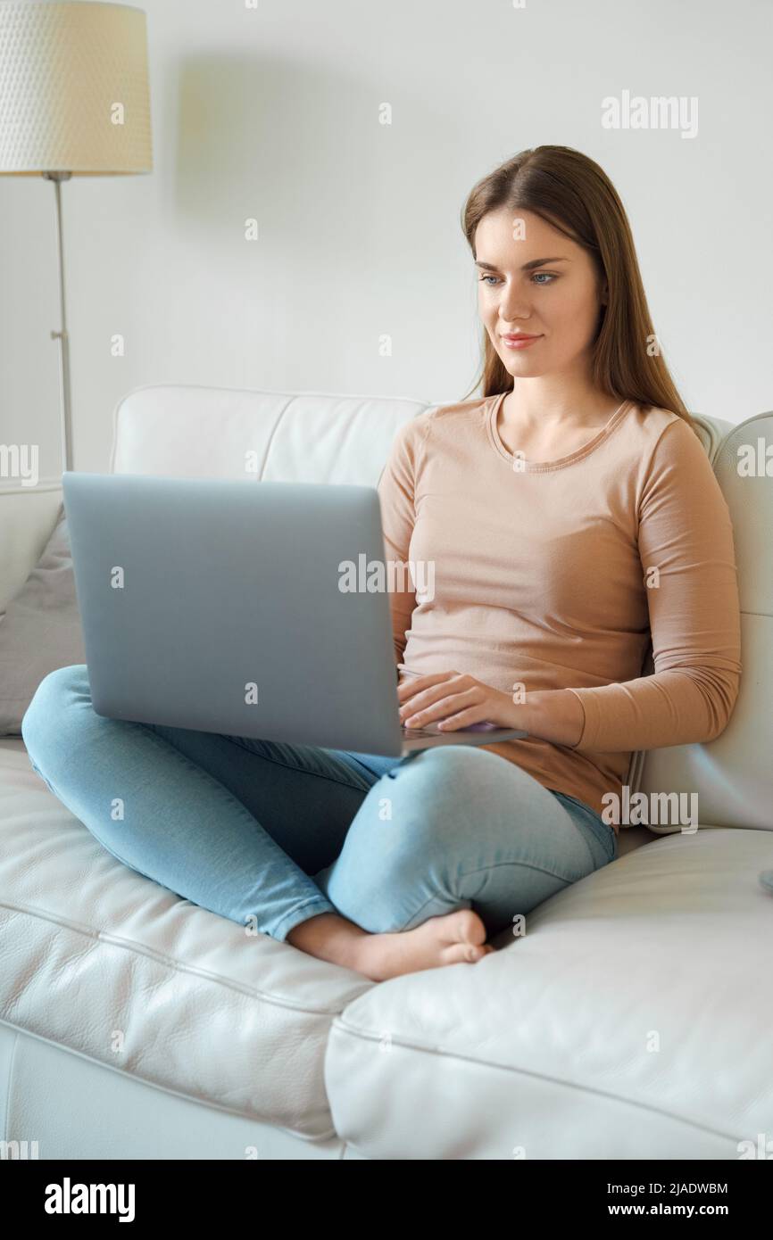 Ganzkörperfoto der jungen Teenager-Frau, die einen Laptop auf dem heimischen Sofa verwendet Stockfoto