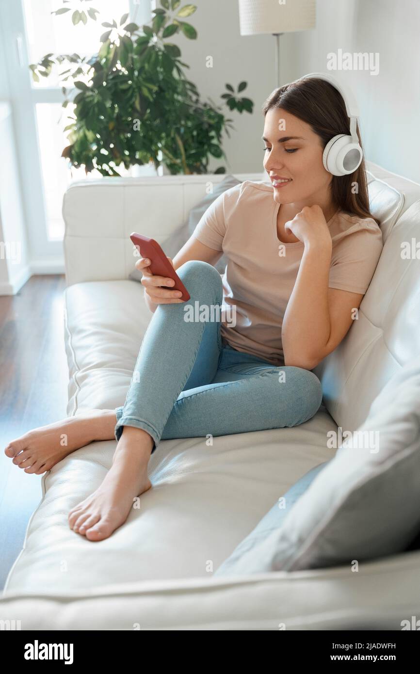 Zufriedene Teenager-Frau, die Medien auf dem Smartphone auf dem Sofa zu Hause sieht Stockfoto