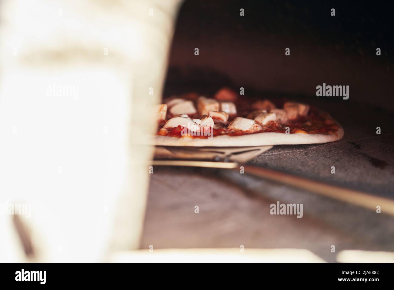 Die Pizza wird zum Backen in einen Holzofen gelegt. Der Prozess der Herstellung von hausgemachter Pizza. Das Konzept der hausgemachten Fast Food. Vorderansicht. Stockfoto