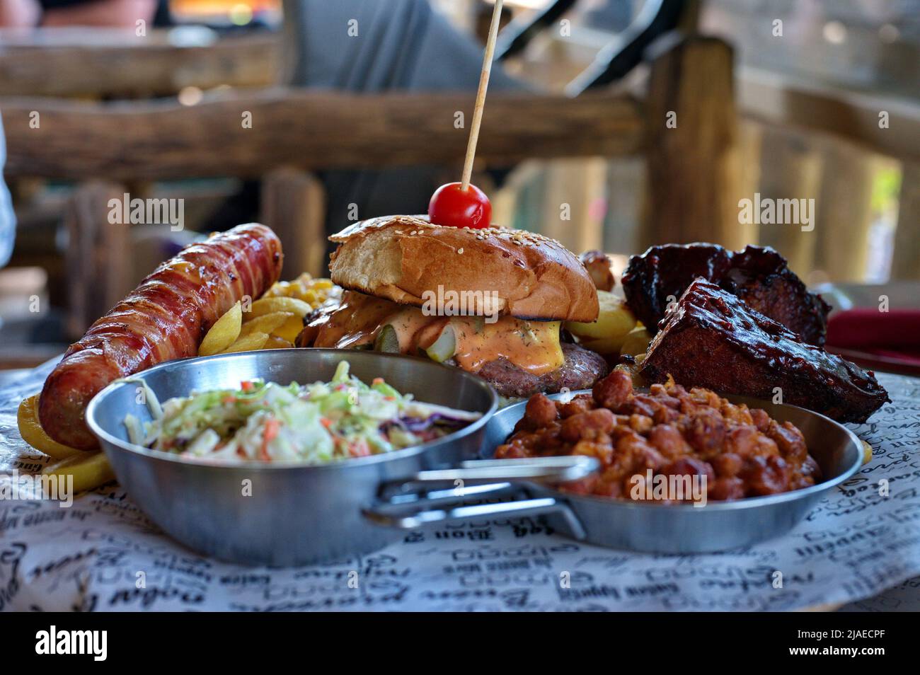 Teller mit Burger, Rippchen und Schweinefleisch mit verschiedenen Salaten auf rustikalem Tisch Stockfoto