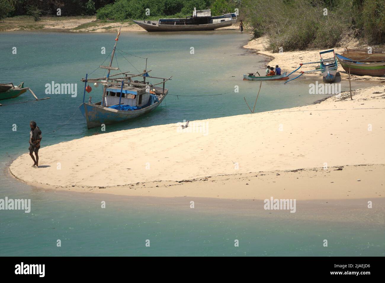 Ein Mann, der am Sandstrand steht, im Hintergrund von Fischerbooten auf einer lagunenartigen Meereslandschaft am Fischerstrand von Pero in Pero Batang Villlage, Kodi, Südwesten Sumba, Ost Nusa Tenggara, Indonesien. Stockfoto