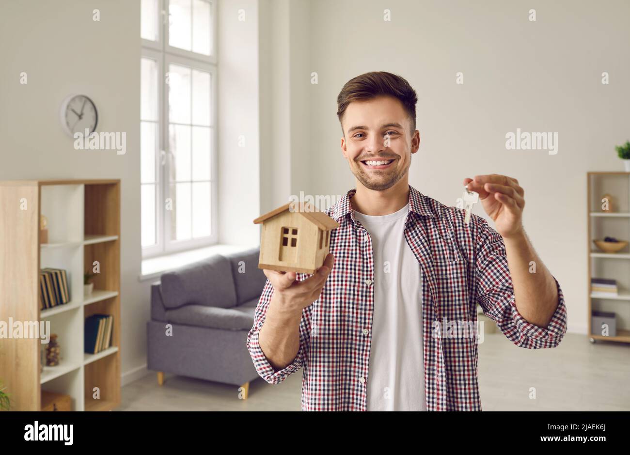 Porträt eines glücklichen jungen Mannes mit einem kleinen Layout aus Holzhaus und mit Schlüsseln in den Händen. Stockfoto