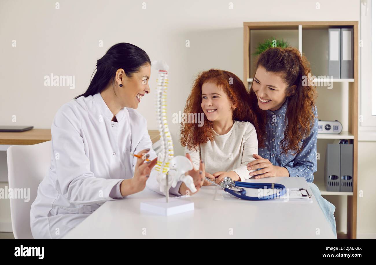 Freundlicher Arzt zeigt kleines Mädchen anatomisches Modell der Wirbelsäule auf dem Tisch in der Arztpraxis stehen. Stockfoto