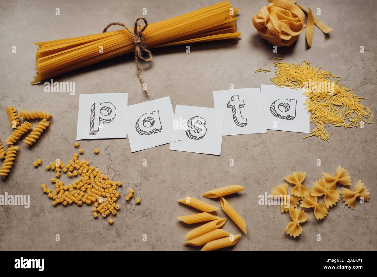 Schriftzug mit verschiedenen Nudelsorten und einer Handvoll Spaghetti auf dem Tisch Stockfoto