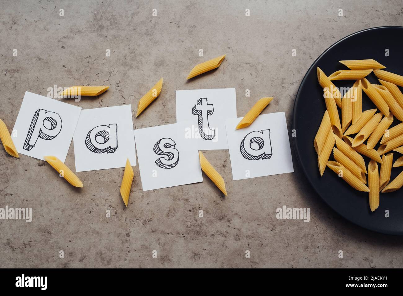 Schriftzug mit einer Handvoll Pasta auf dem schwarzen Teller auf dem Tisch Stockfoto