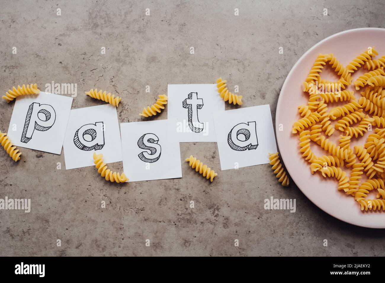 Schriftzug mit Wavy Pasta auf dem rosafarbenen Teller auf dem Tisch Stockfoto