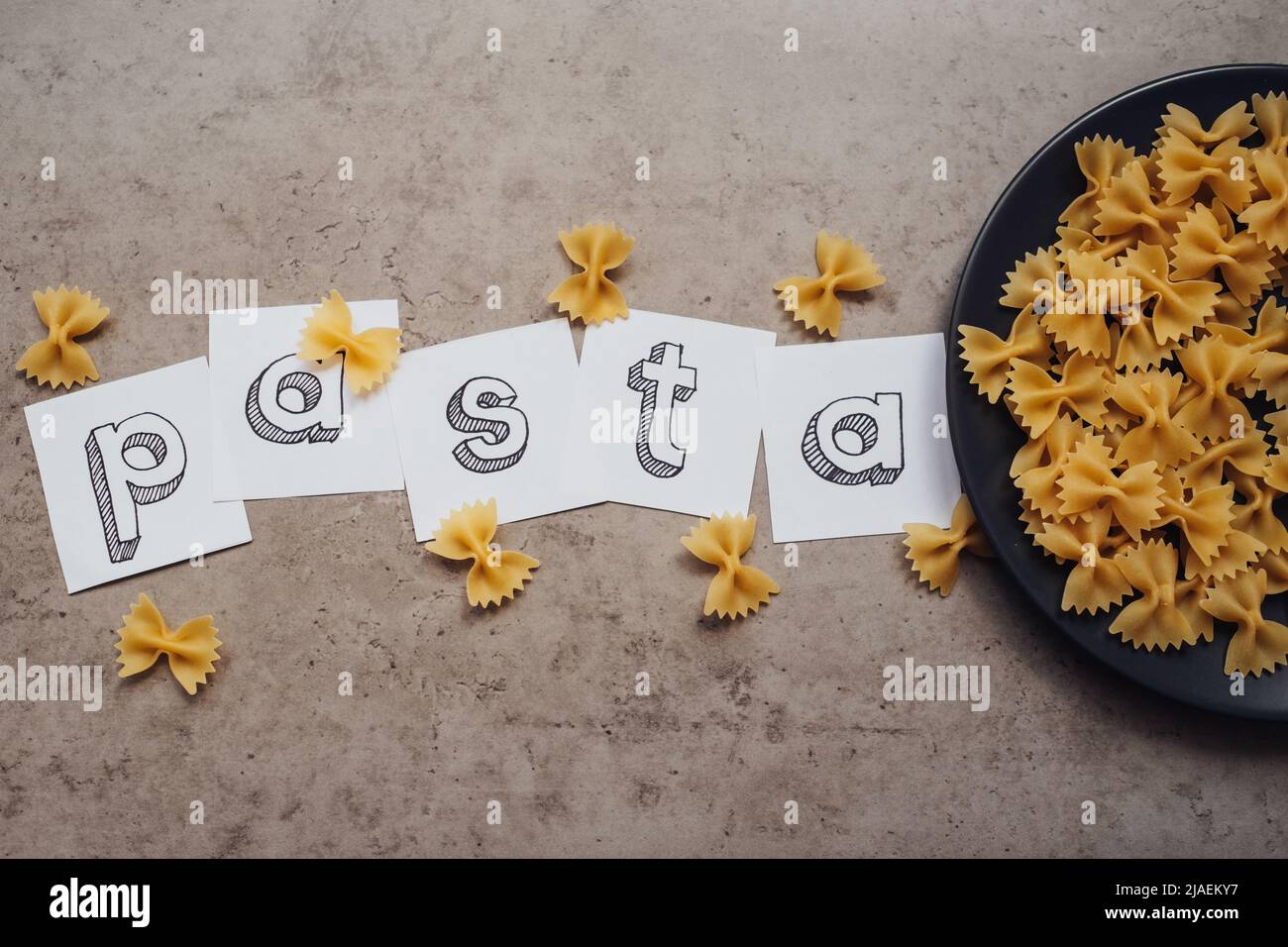 Schriftzug mit einer Handvoll Pasta auf dem schwarzen Teller auf dem Tisch Stockfoto