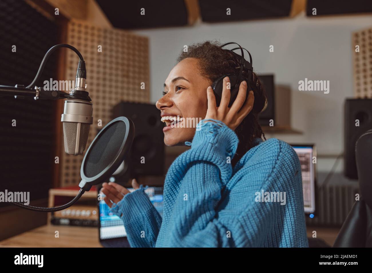 Lustige junge multiethnische Anchor Frau Moderatorin spricht ins Mikrofon, nimmt Audio-Podcast im professionellen Aufnahmestudio auf Stockfoto