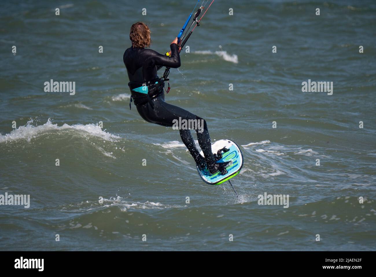 Männlicher Kite Foil Surfer mit langen Haaren auf dem Meer. Rückansicht aus der Nähe Stockfoto