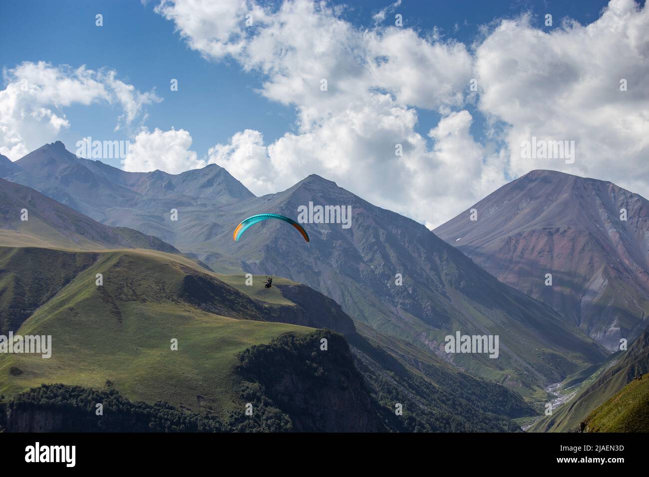 Ein Mann auf einem Gleitschirm macht ein Selfie. Bergschlucht mit grünen Hängen, ein Fallschirm mit Menschen fliegt über die Klippe. Wunderschöne Aussicht auf die Panoramalandschaft Stockfoto