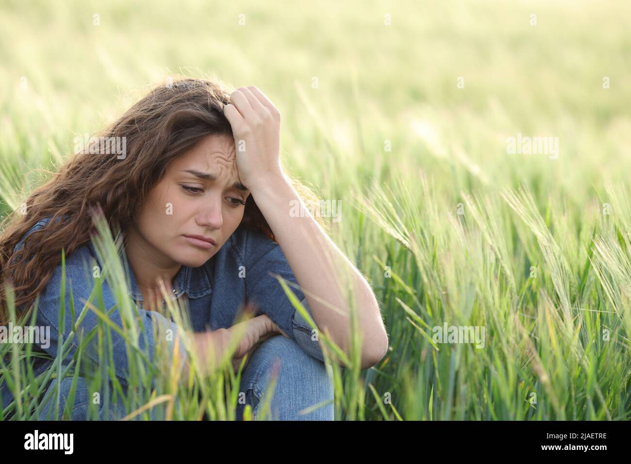 Traurige Frau, die sich beschwert, allein auf einem Feld zu sitzen Stockfoto
