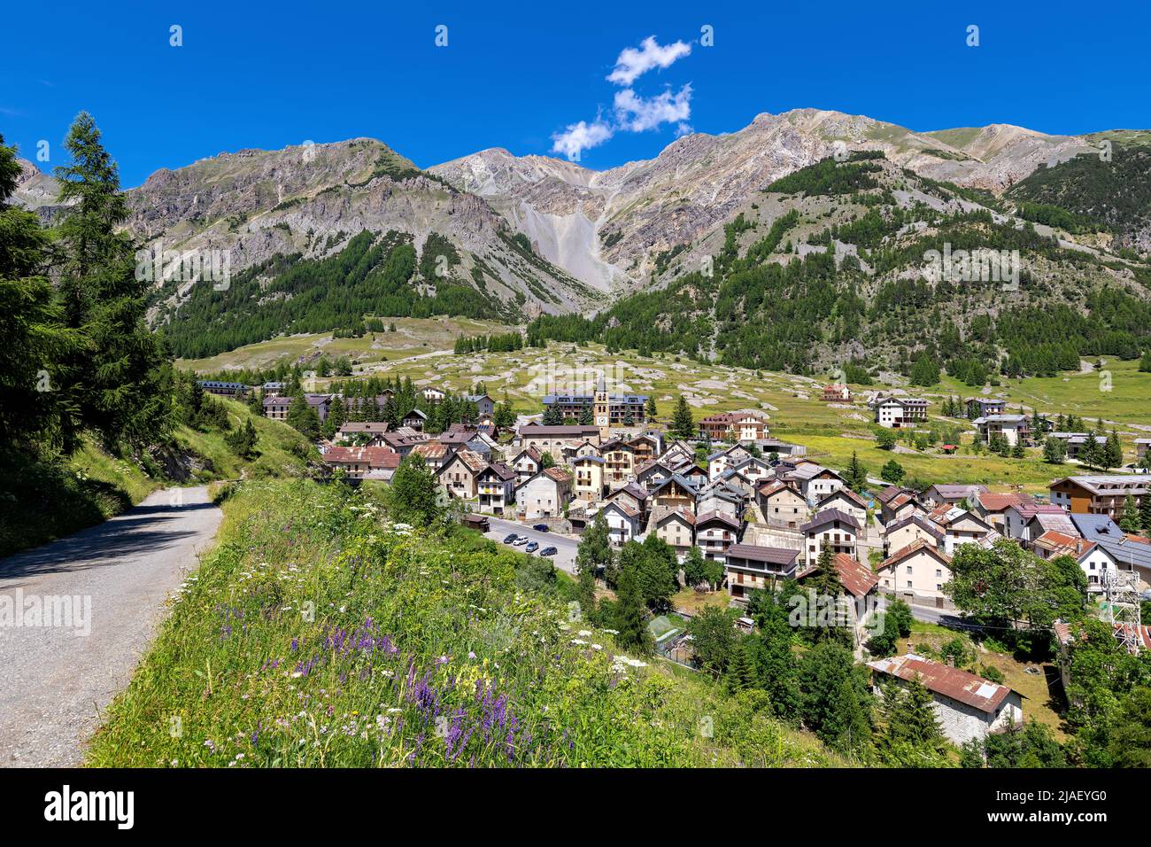 Ländliche Straße und kleine alpine Stadt Bersezio auf dem grünen Tal zwischen Bergen unter blauem Himmel in Piemont, Norditalien. Stockfoto