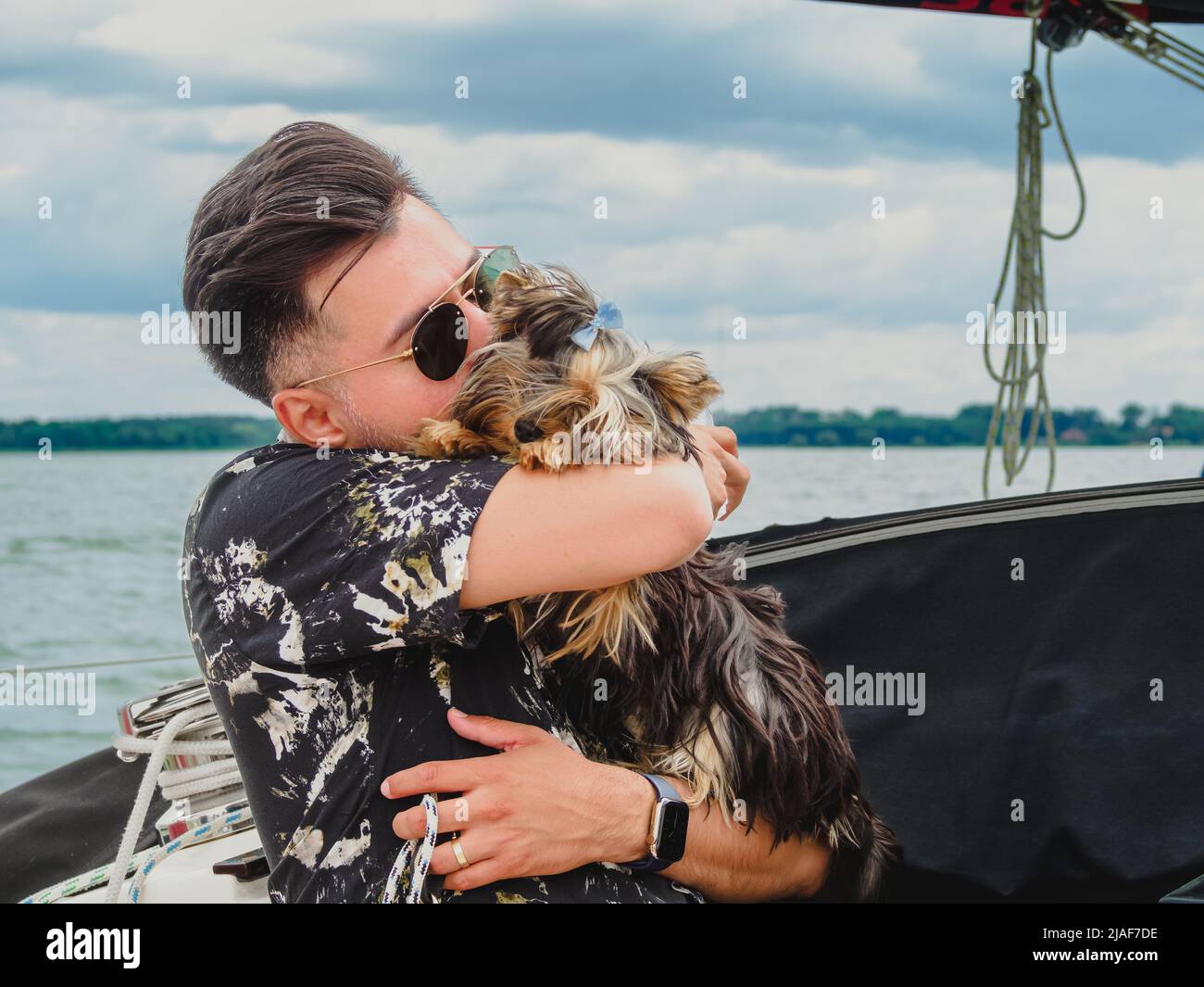 Ein hübscher Mann umarmt und küsst seinen kleinen Hund yorkshire Terrier Stockfoto