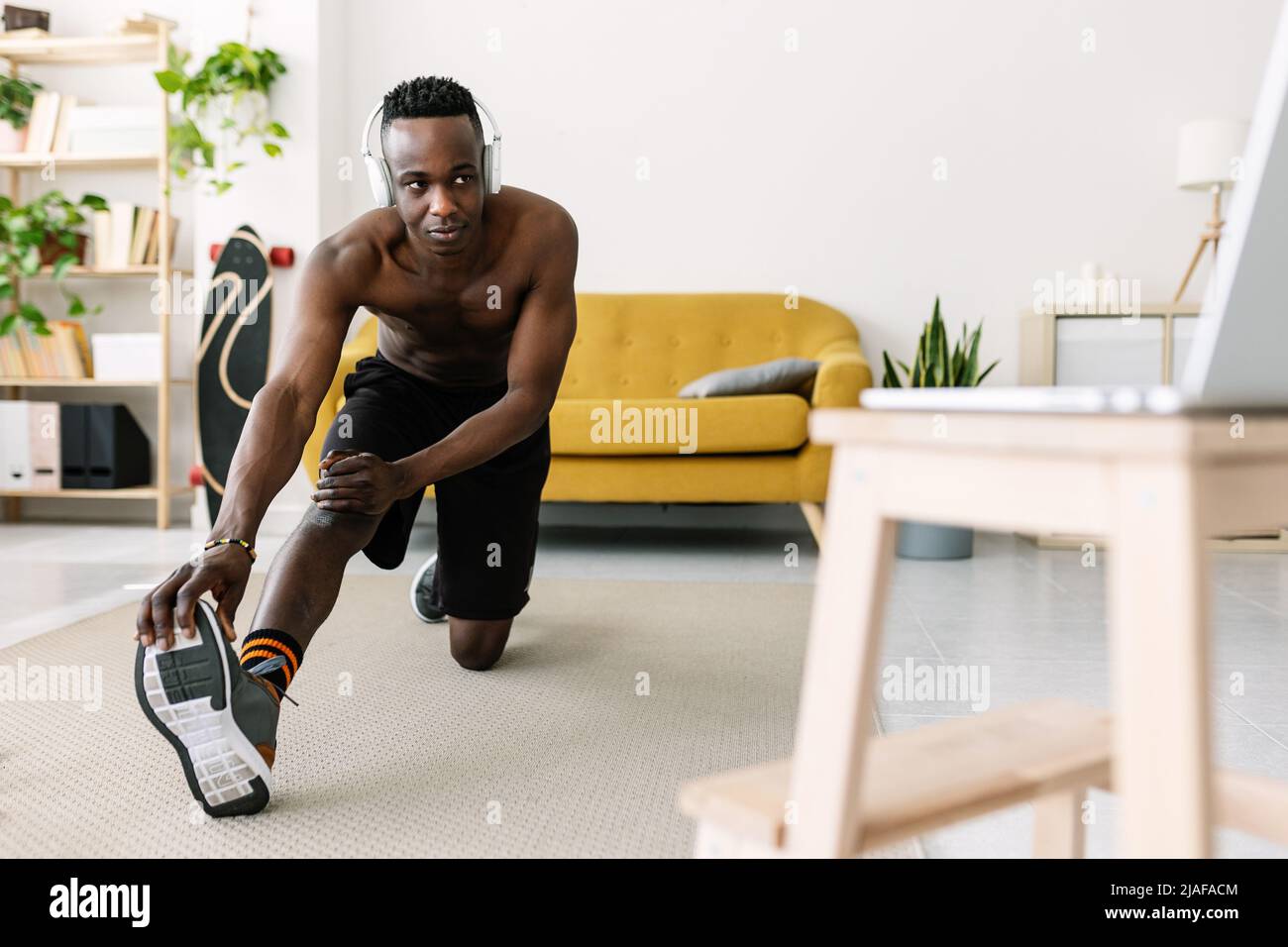 Junger erwachsener afrikanischer Mann trainiert und dehnt sich während er sich ein Fitnessvideo ansieht Stockfoto