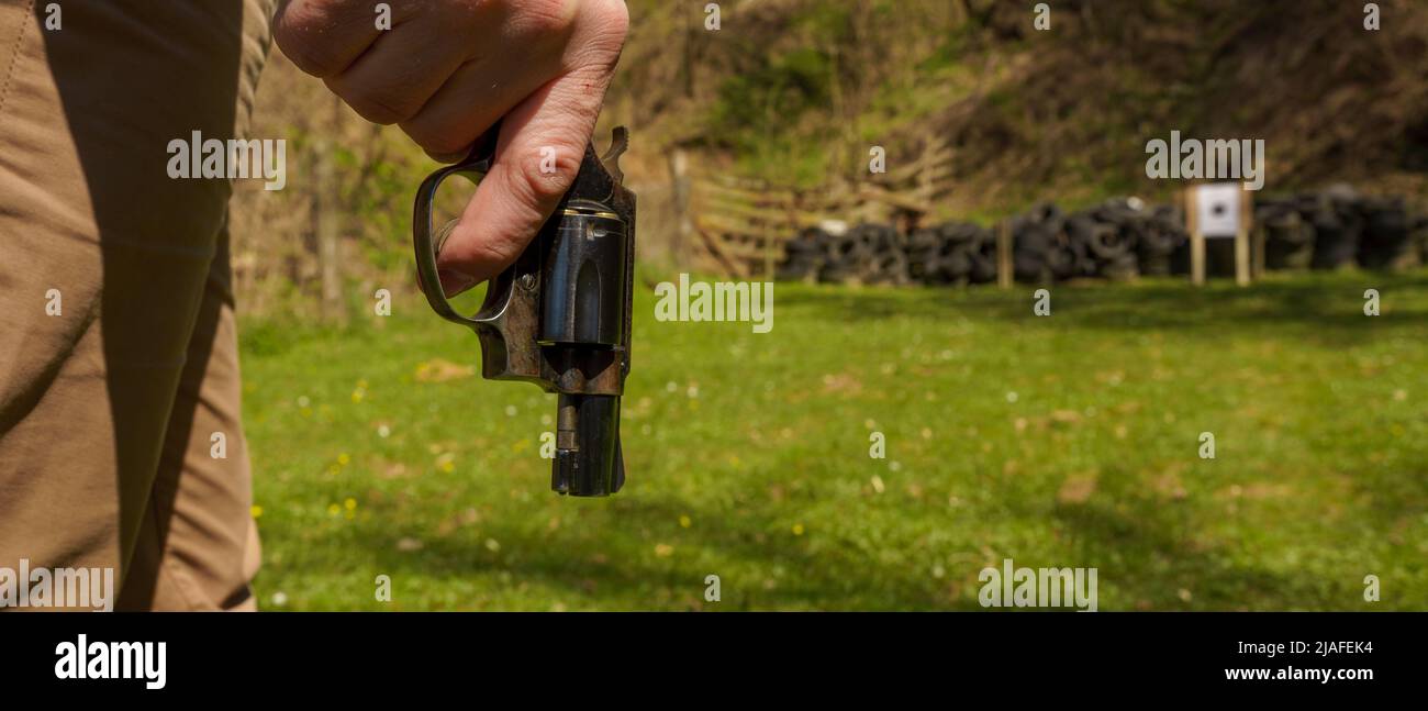 Nicht erkennbarer Mann mit Revolver, der sich darauf vorbereitet, das Ziel auf dem Schießstand im Freien zu schießen. Stockfoto