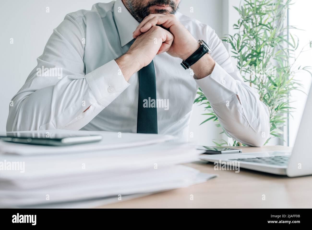 Kontemplativer Geschäftsmann, der sich mit den Händen im Büro am Kinn hält, die Geschäftsaktivitäten sorgfältig plant, selektiver Fokus Stockfoto