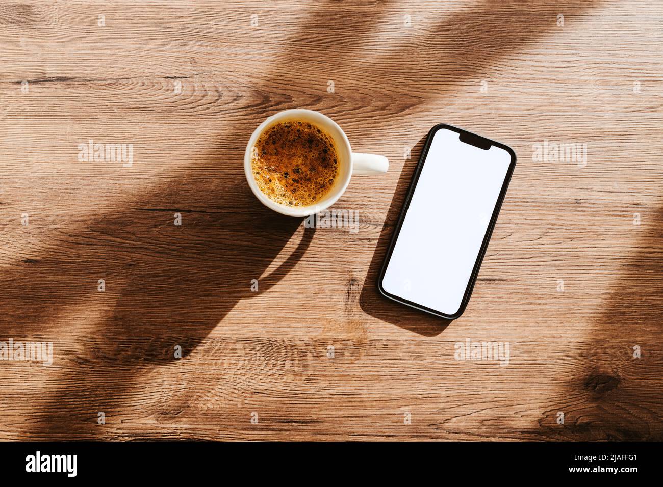 Tasse Kaffee und Smartphone mit leerem weißen Mockup-Bildschirm auf dem Schreibtisch des Heimbüros, Flachlagerung von oben Stockfoto