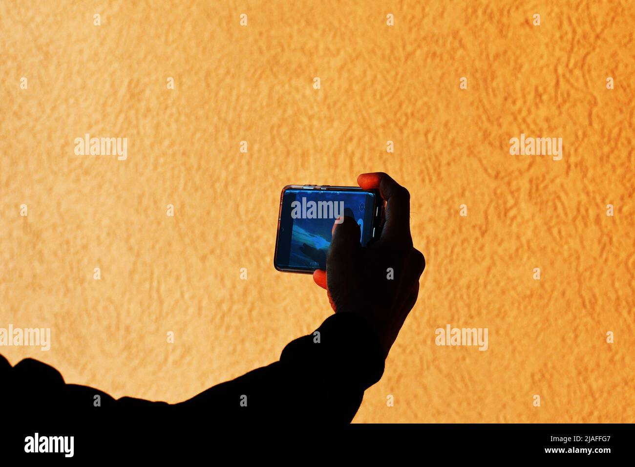 SELFIE: Eine Steinmauer auf dem Balkon eines Hotelzimmers beleuchtet Bernstein, wie ein Mann sich und den Sonnenaufgang hinter ihm fotografiert. Stockfoto
