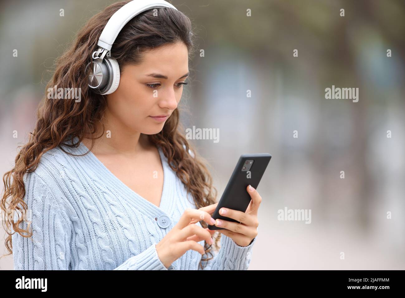 Eine seriöse Frau mit kabellosen Kopfhörern, die Musik hört und ihr Smartphone auf der Straße abhört Stockfoto