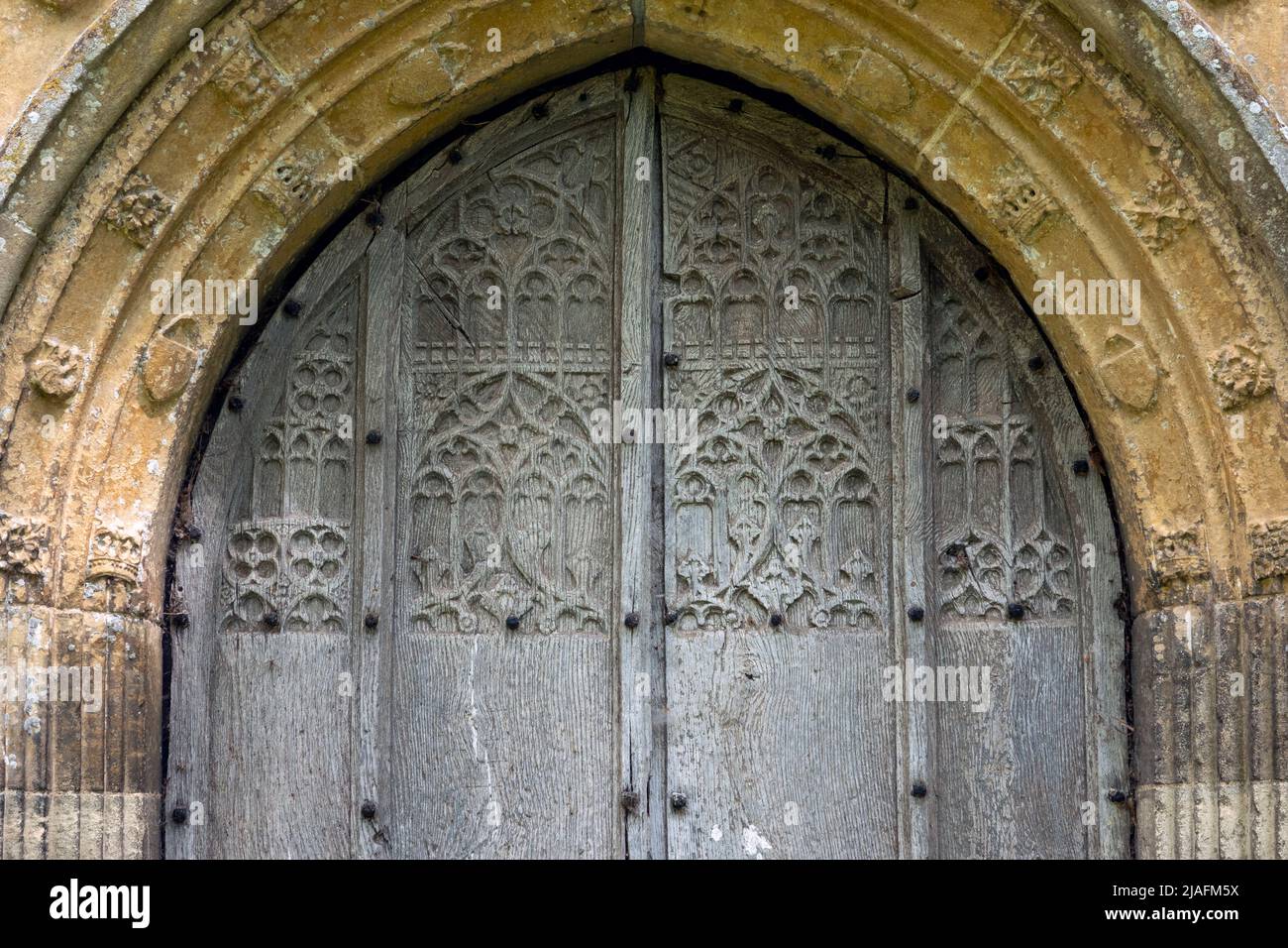 Fein geschnitzte Holztür in dekorativem Steingewölbe in einer flushwork-Feuerstein-Wand, All Saints Church, Brandeston, Suffolk Stockfoto