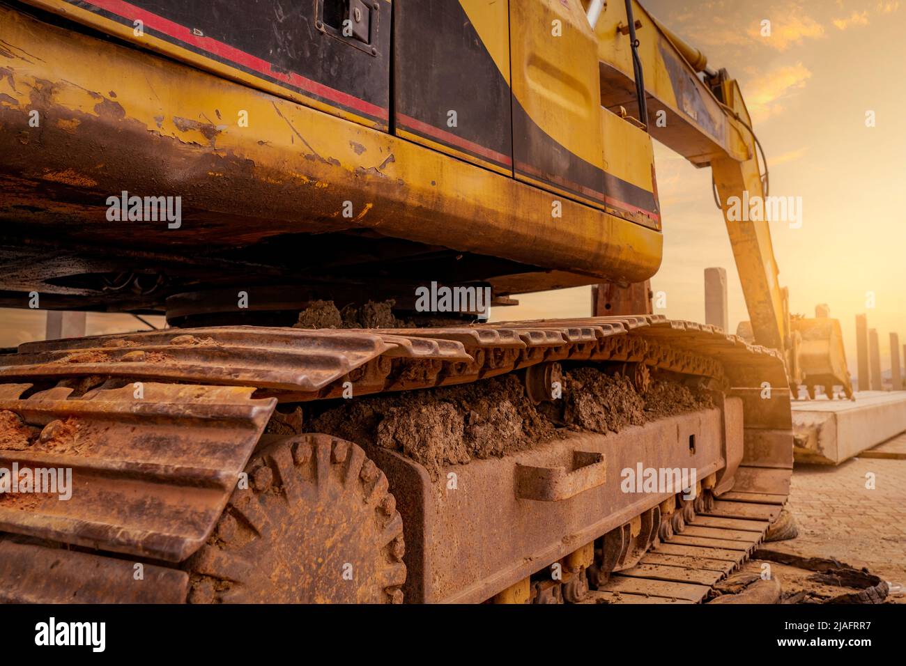 Nahaufnahme der Schotterpanzer der Bagger. Bagger auf der Baustelle geparkt. Bulldozer in der Nähe von Betonmast. Maschine mit Erdbewegung. Gelber Bagger mit Eimer. Stockfoto
