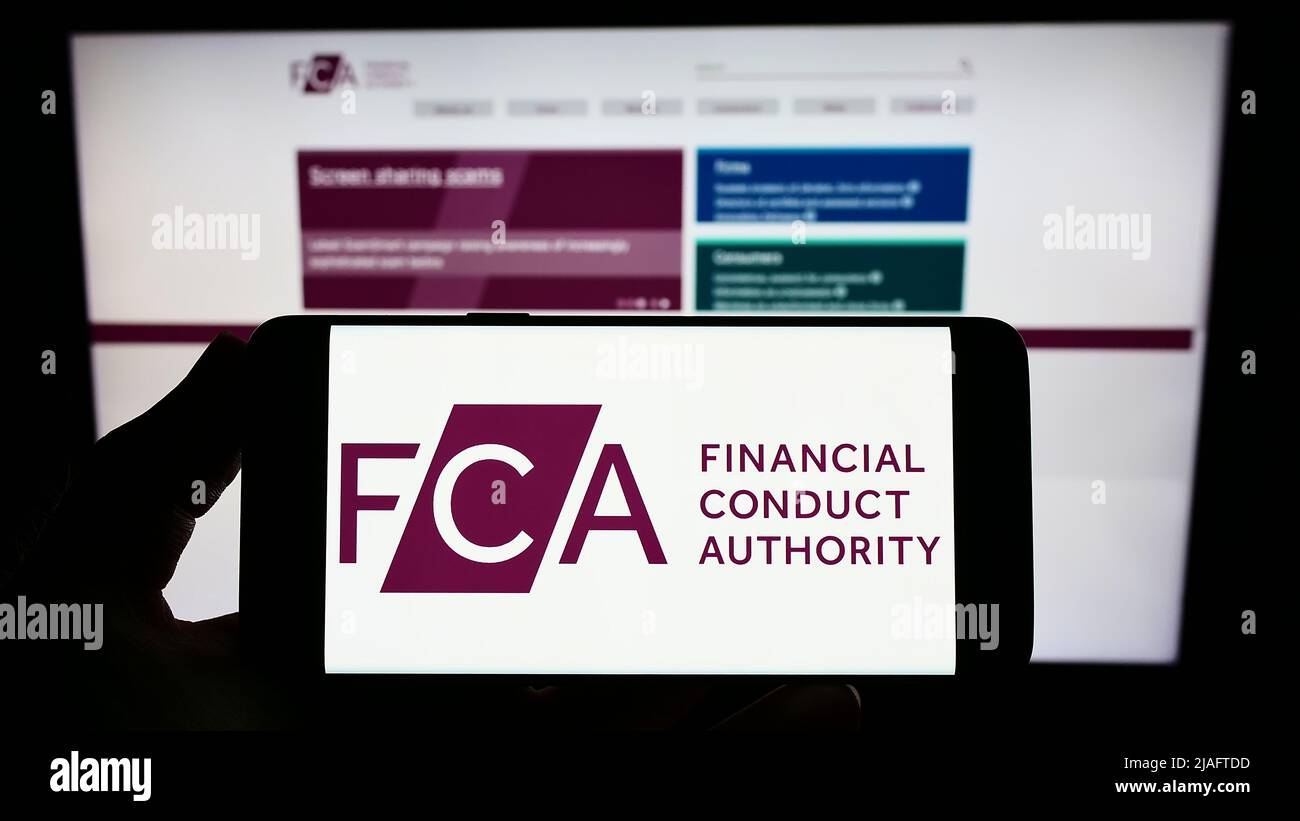 Person, die das Smartphone mit dem Logo der British Financial Conduct Authority (FCA) auf dem Bildschirm vor der Website hält. Konzentrieren Sie sich auf die Telefonanzeige. Stockfoto