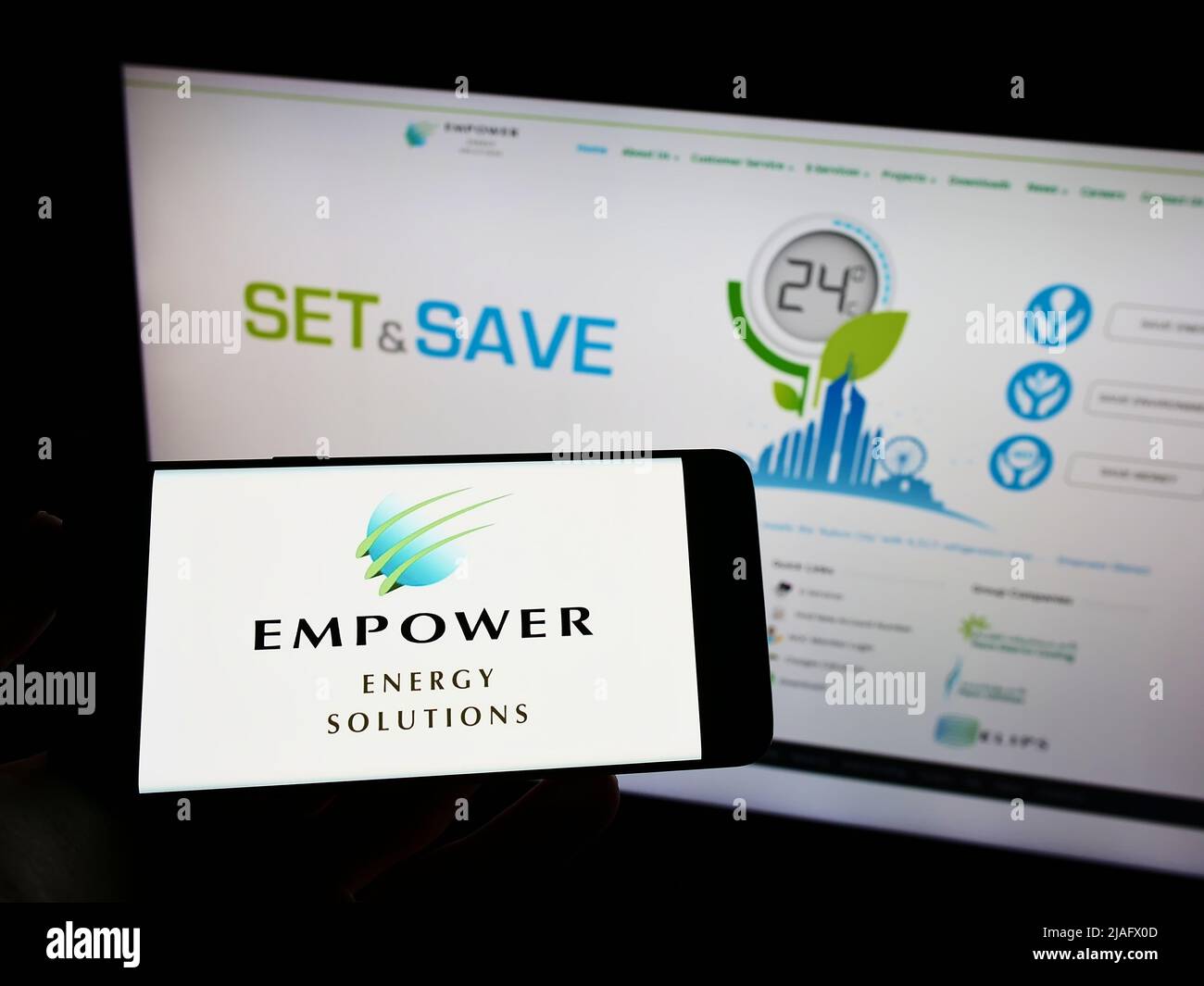 Person, die das Mobiltelefon mit dem Logo der Firma Emirates Central Cooling Systems (Empower) auf dem Bildschirm vor der Website hält. Konzentrieren Sie sich auf die Telefonanzeige. Stockfoto