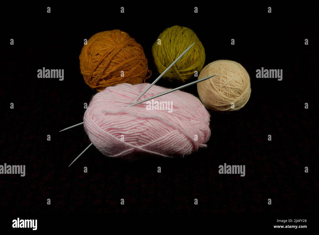 Bunte Garnknäuel und Stricknadeln auf schwarzem Hintergrund Stockfoto