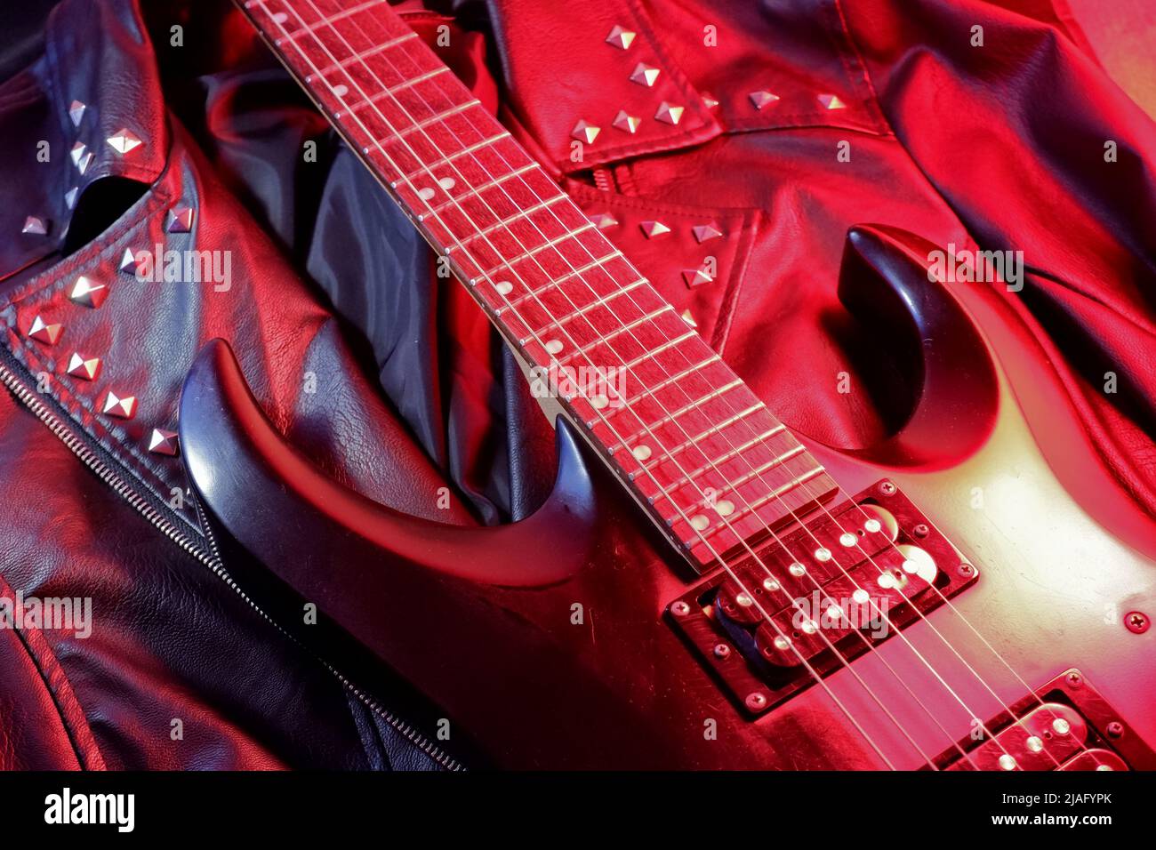 E-Gitarre auf einer rot beleuchteten Lederjacke Stockfoto