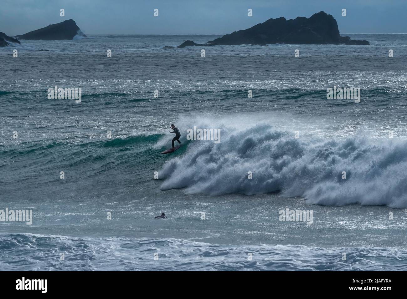Spektakuläre Surfing-Action als Surfer reitet auf dem Kamm einer Welle bei Fistral mit der felsigen Insel The Goose im Hintergrund in Newquay in Cornwall i Stockfoto
