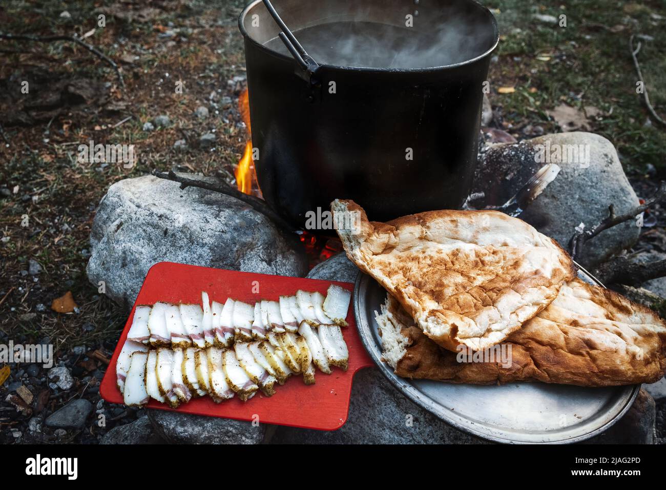 Dunkler großer Topf oder Kessel, Kochtopf mit kochendem Wasser im Inneren über dem Feuer irgendwo im Park oder in den Bergen, Campingkonzept Stockfoto