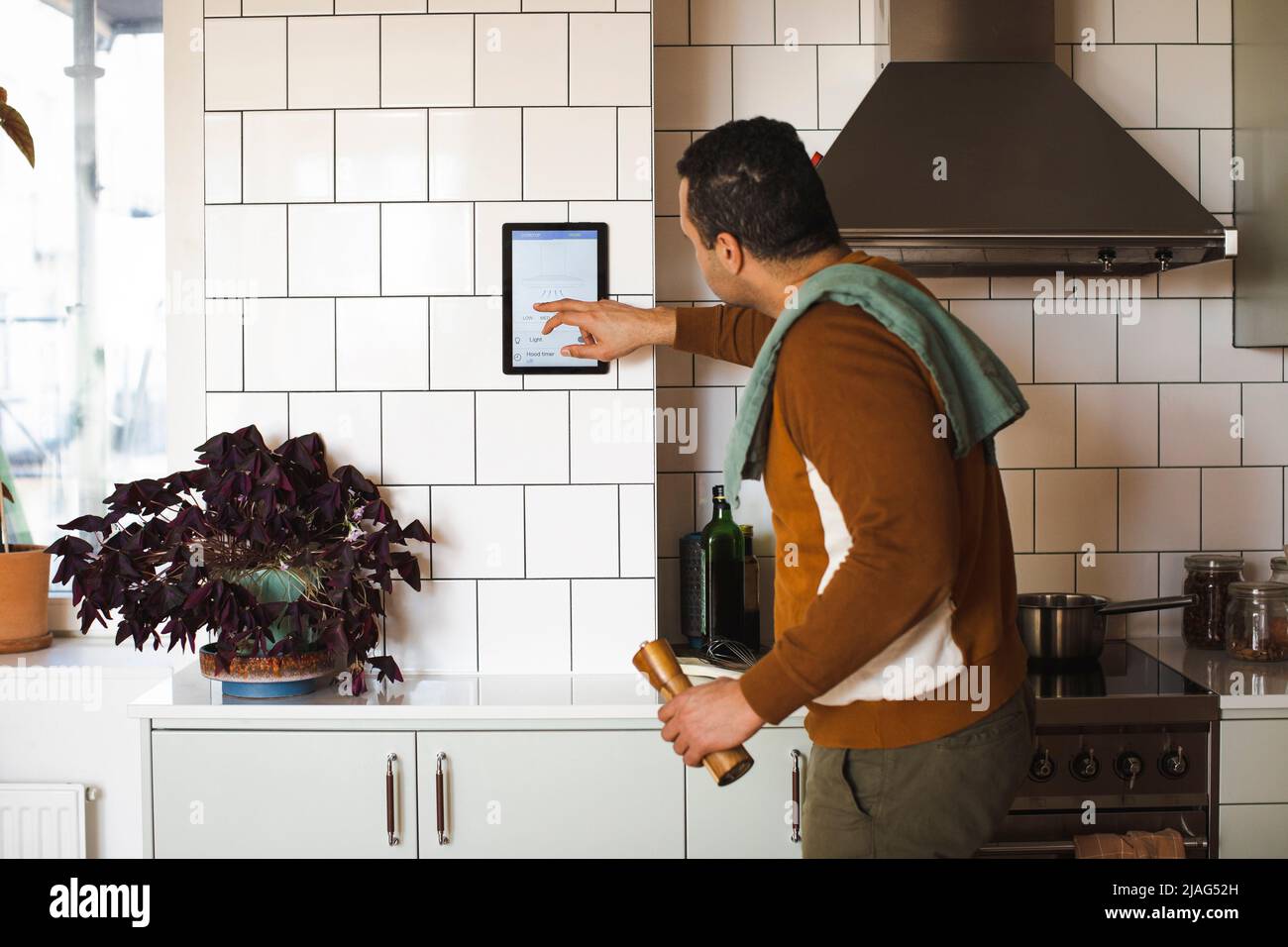 Seitenansicht des Mannes, der ein Hausautomationsgerät an der Wand verwendet, während er zu Hause in der Küche steht Stockfoto