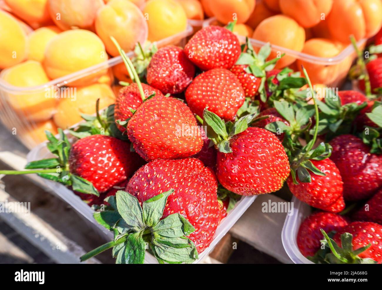Frische reife Erdbeeren und Aprikosen in Plastikboxen auf dem lokalen Bauernmarkt Stockfoto
