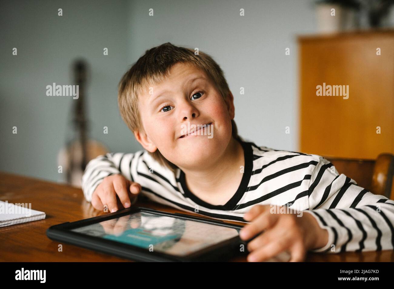 Porträt eines glücklichen Jungen mit Down-Syndrom, der am Tisch sitzt Stockfoto