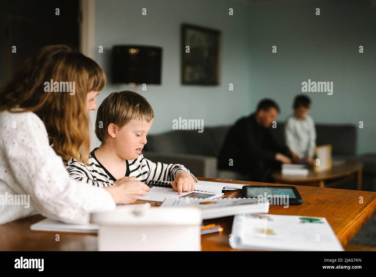 Junge mit Down-Syndrom liest Buch von der Mutter, während Hausaufgaben am Tisch Stockfoto