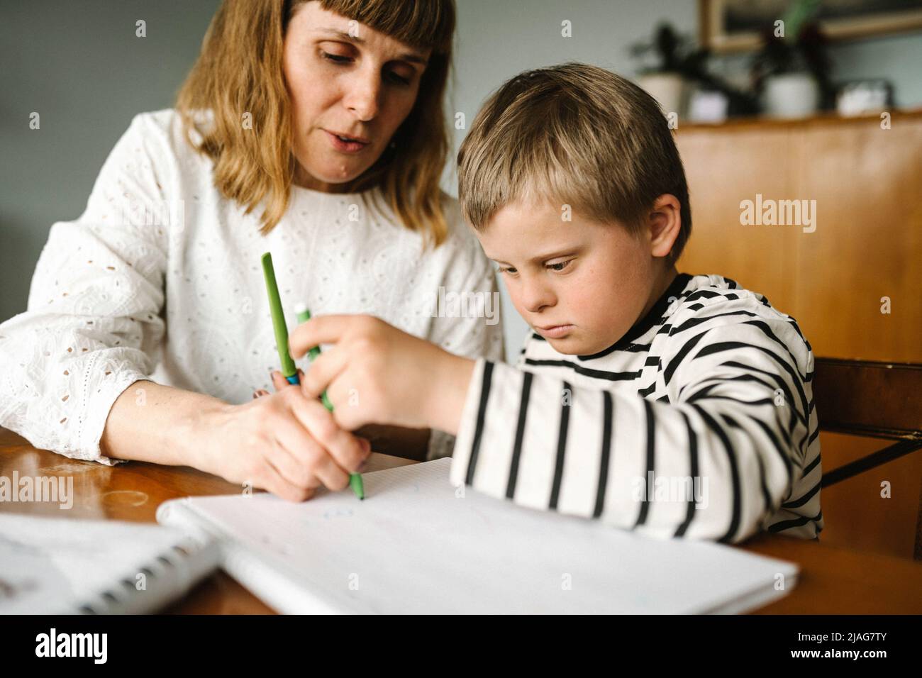 Junge mit Behinderung, der die Mutter unterstützt, während er zu Hause Buch zeichnet Stockfoto