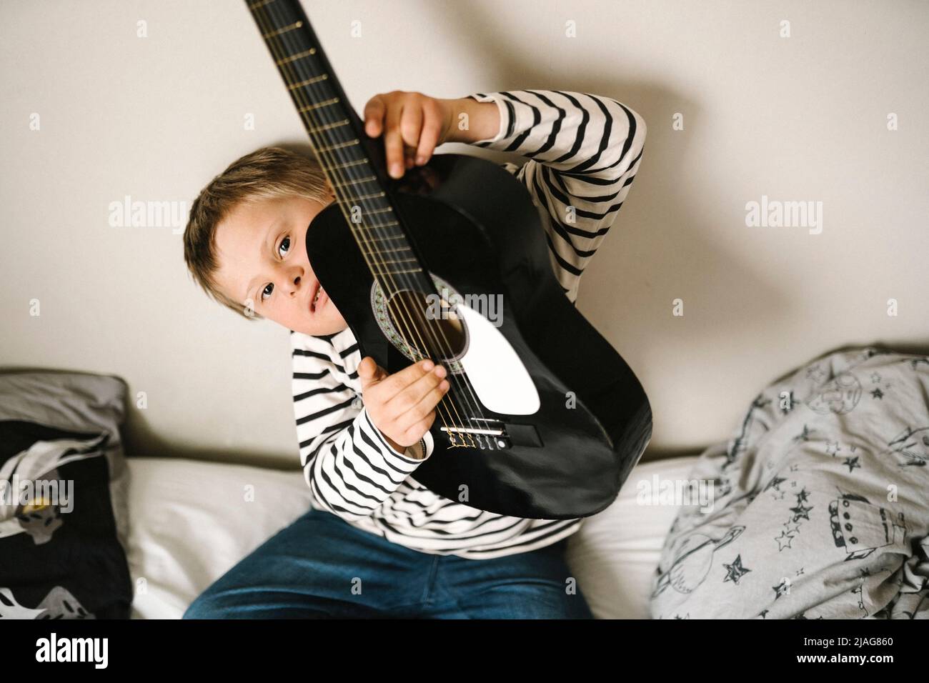 Porträt eines Jungen mit Down-Syndrom, der Gitarre im Schlafzimmer hält Stockfoto