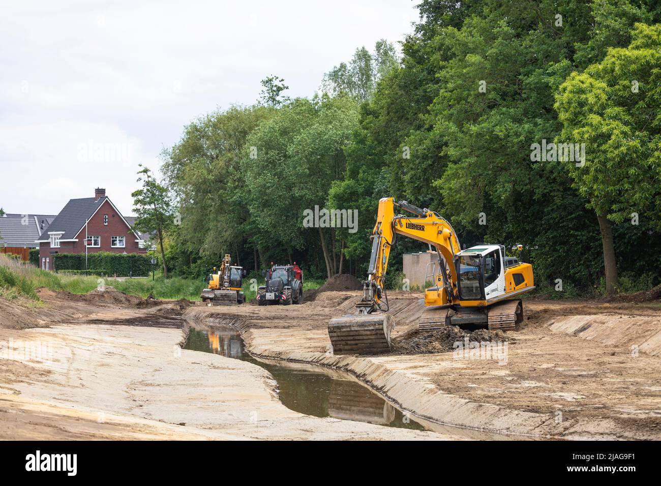 Bagger bei der Arbeit Wiederherstellung kanalisierten Streamlet wieder in mäandernde Form in einem Wohngebiet, Wasserwirtschaft in den Niederlanden Stockfoto