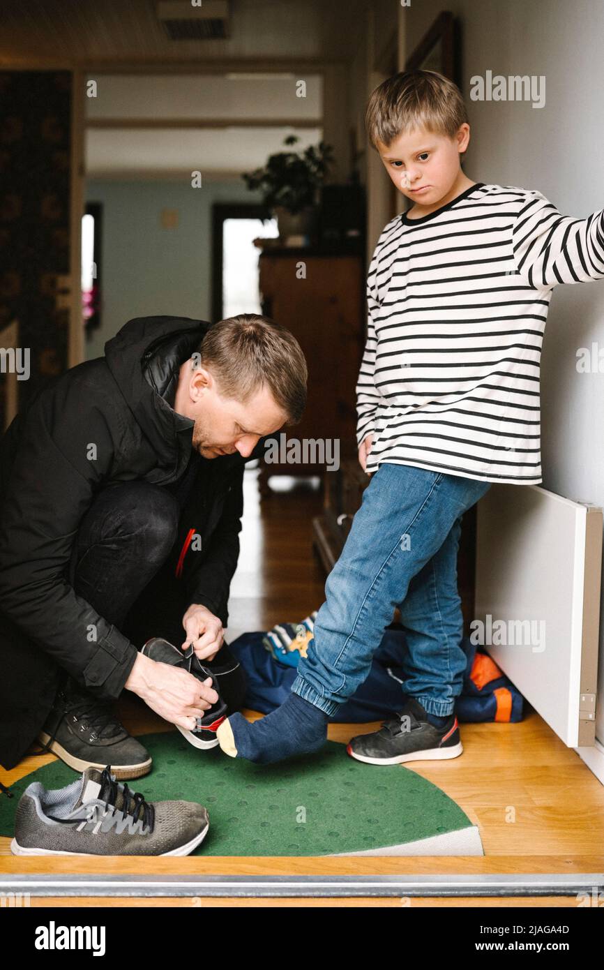 Vater hilft Sohn mit Behinderung, Schuhe zu tragen, die vor der Tür stehen Stockfoto