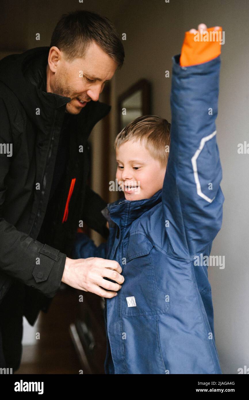 Vater hilft Sohn mit Down-Syndrom, Jacke zu Hause zu tragen Stockfoto