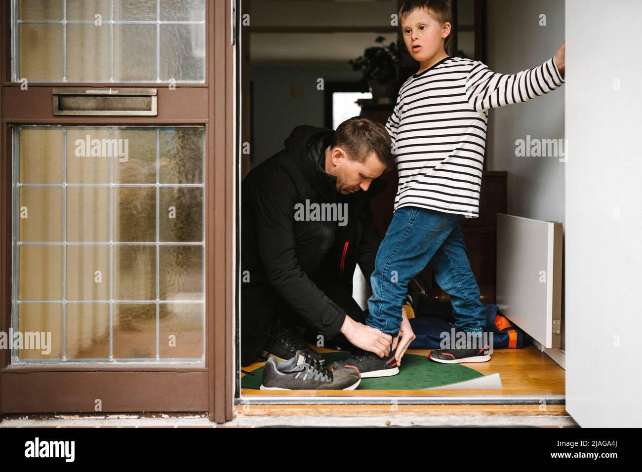 Vater hilft Sohn mit Down-Syndrom, Schuhe zu tragen, die vor der Tür stehen Stockfoto