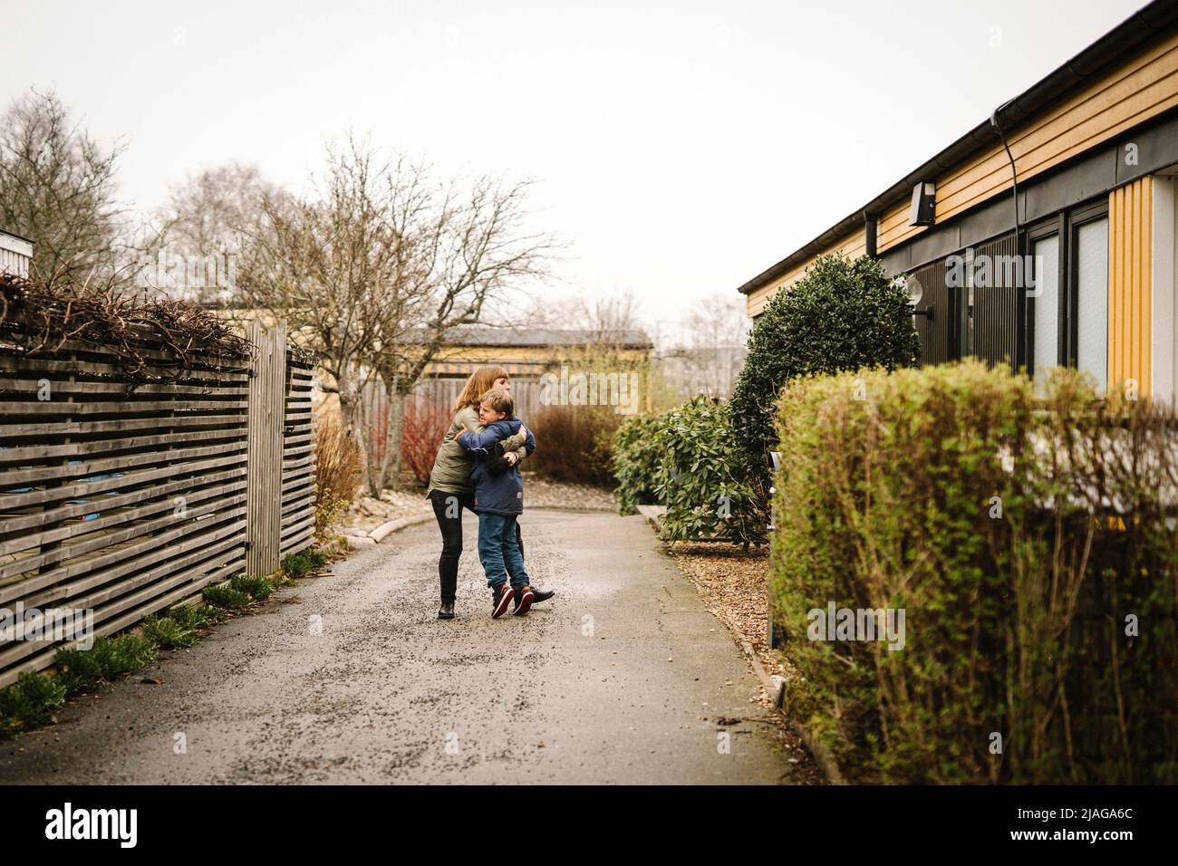 Mutter umarmt Sohn mit Down-Syndrom, während sie zu Hause auf der Straße steht Stockfoto