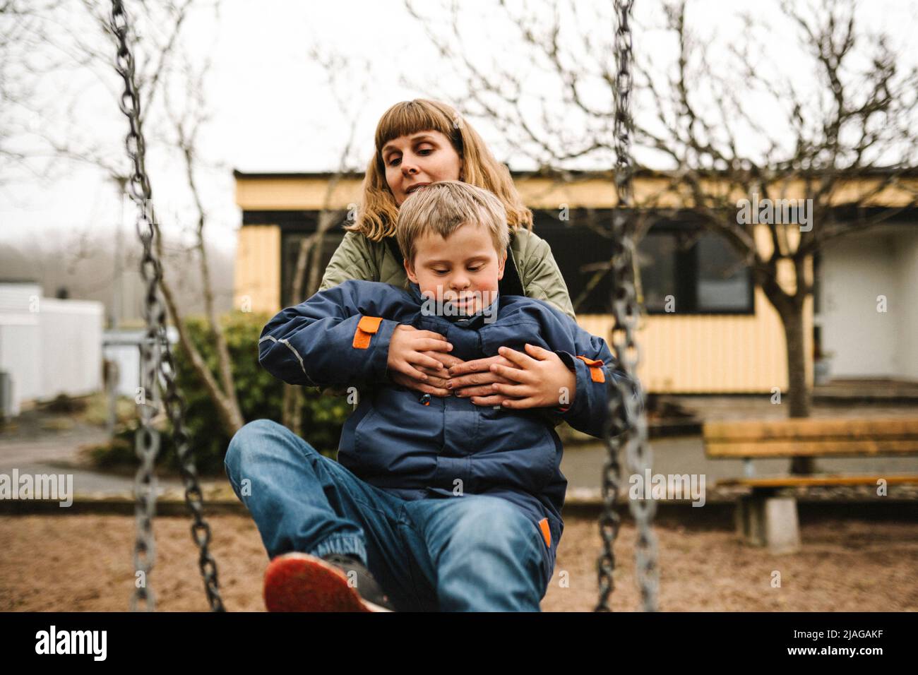 Sohn mit Down-Syndrom, der Mutter hilft, während er im Schaukel im Park sitzt Stockfoto