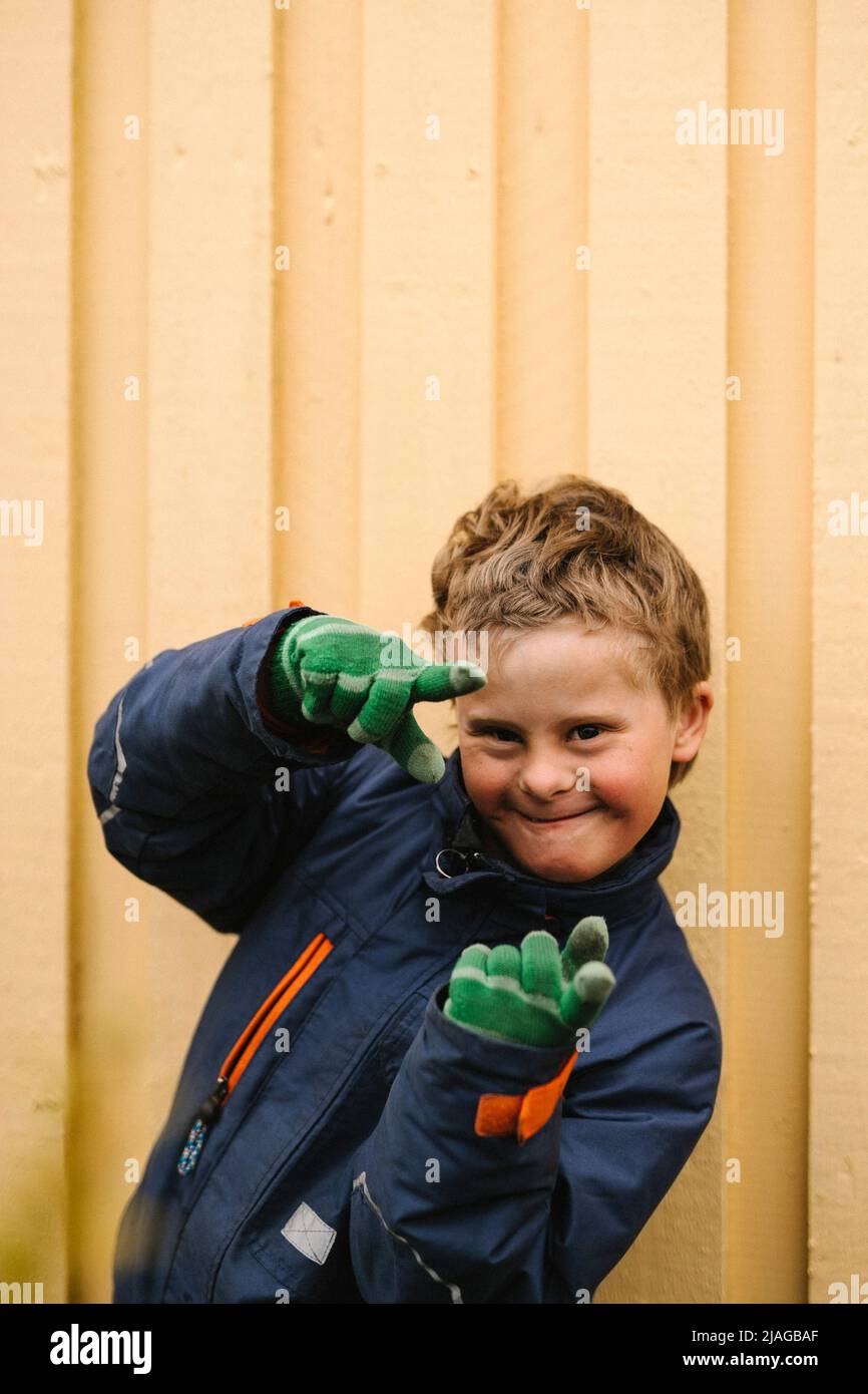 Porträt eines lächelnden Jungen mit Behinderung, der eine Geste des Fingerrahmens an die Wand macht Stockfoto
