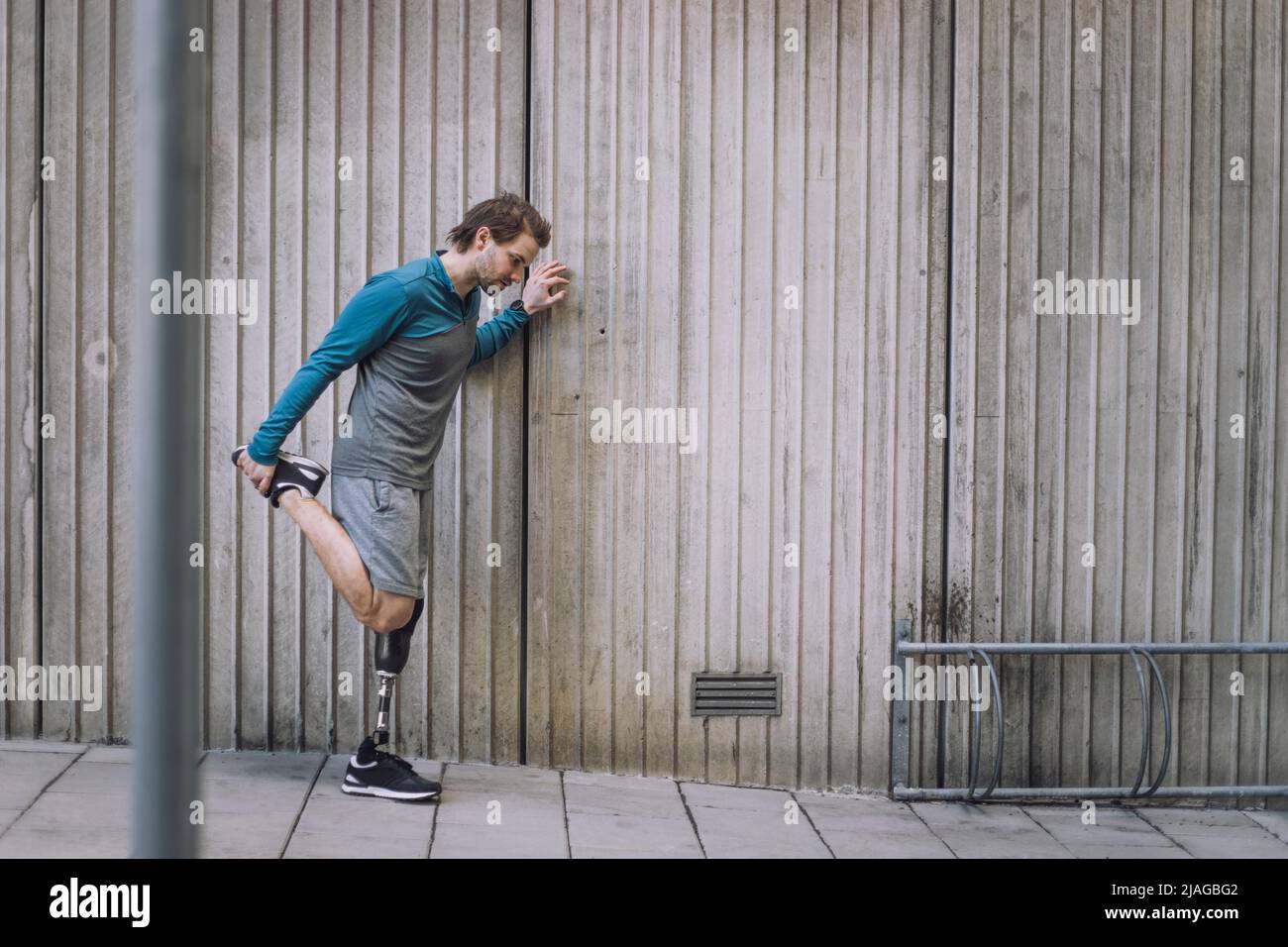 Die ganze Länge des behinderten Mannes, der das Bein streckt, während er an der Wand auf dem Fußweg trainiert Stockfoto