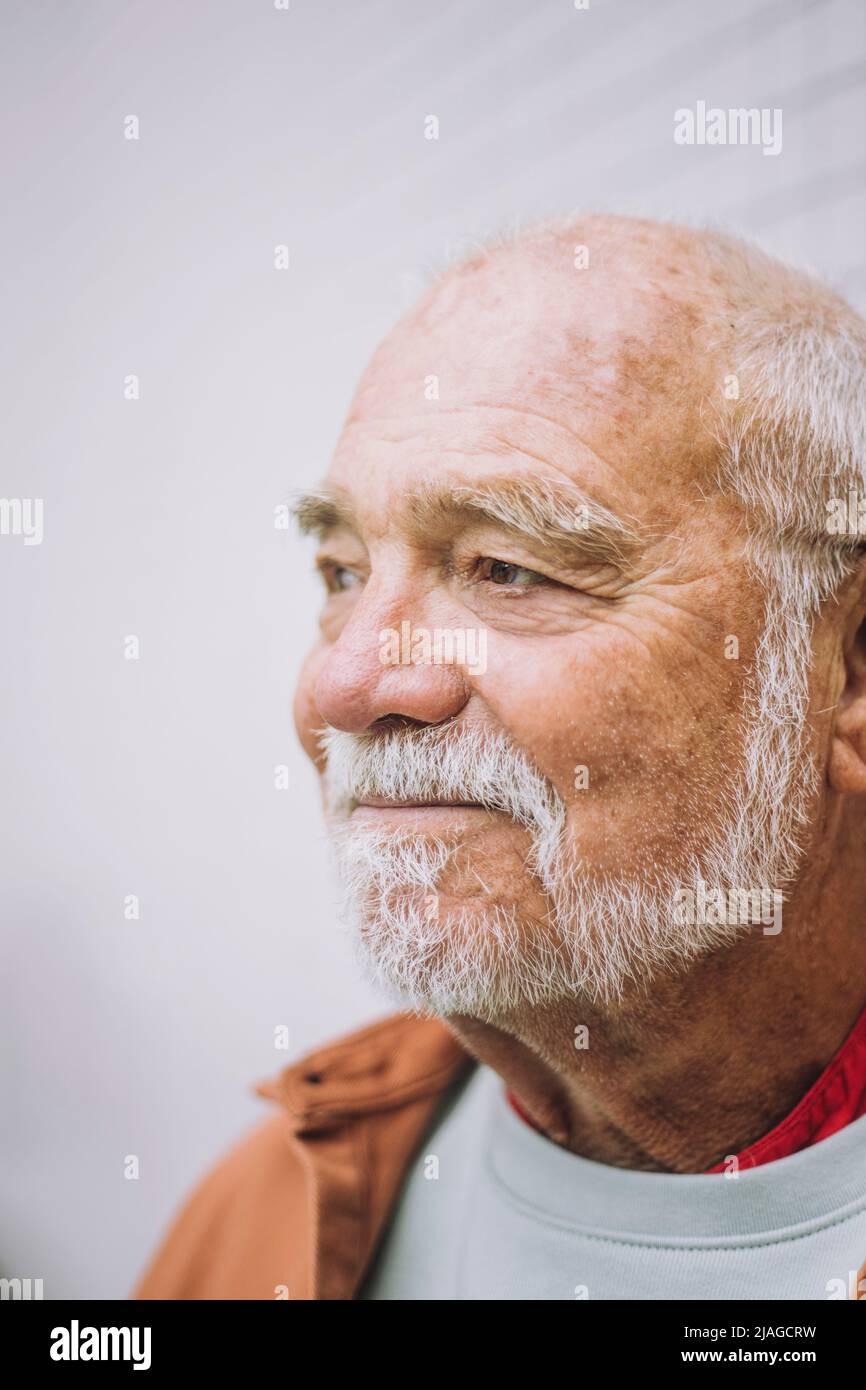 Nachdenklicher älterer Mann, der vor weißem Hintergrund wegschaut Stockfoto
